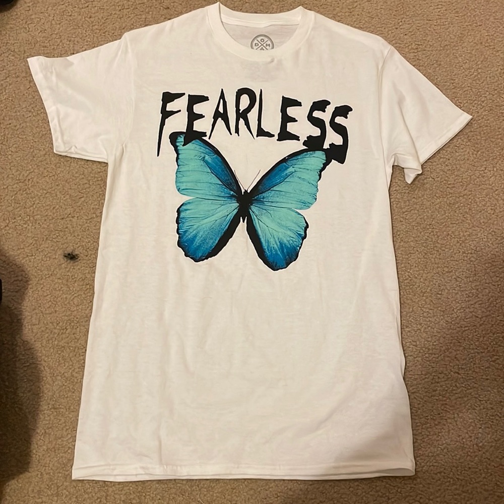 White shirt, with FEARLESS written on it above a butterfly. It is a size S